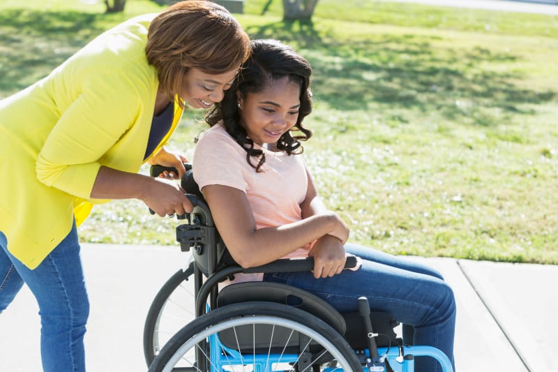 Teenage Daughter in wheelchair being helped by Mother outside.