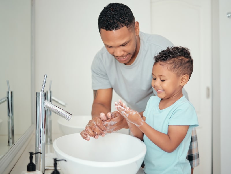 Father teaching Son to wash hands in bathroom.