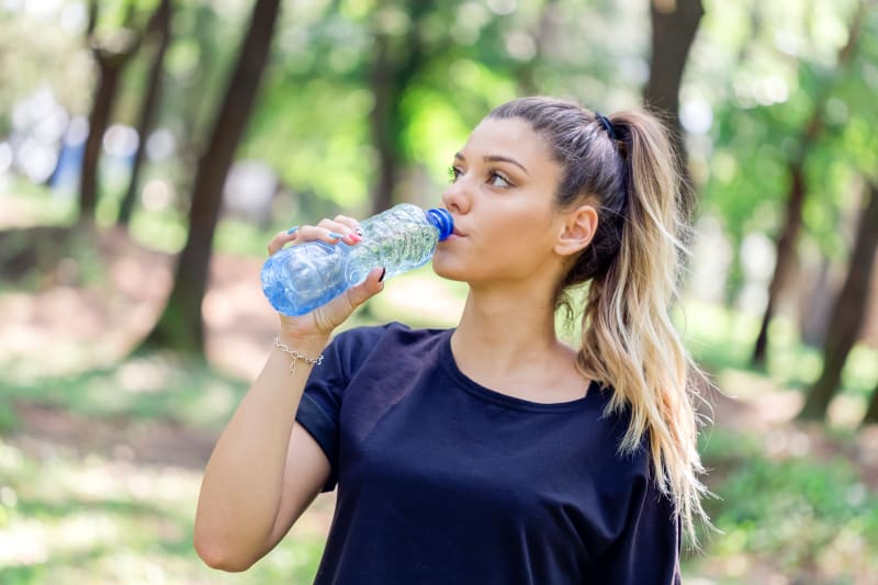 A teenager drinking water outdoors.