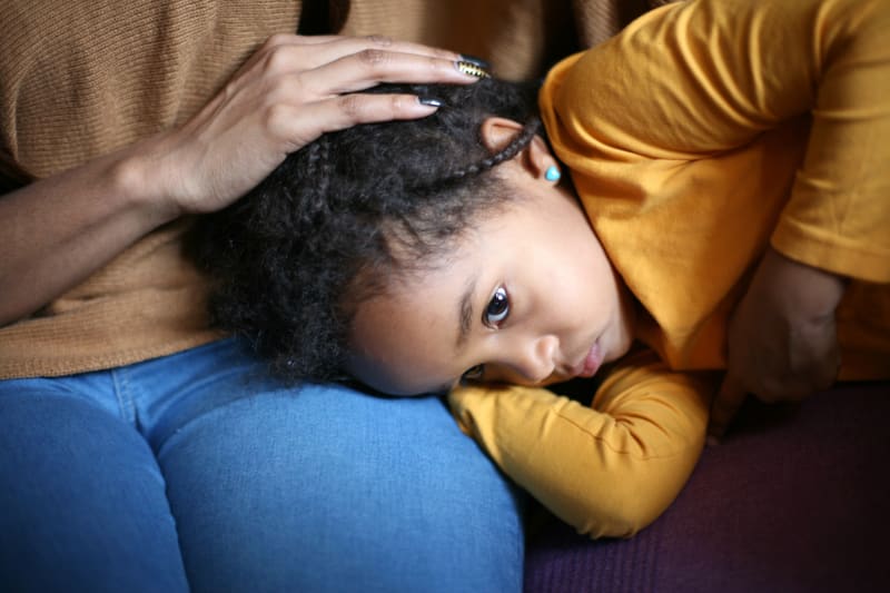 Tired young girl laying on couch resting head on mother's lap. 