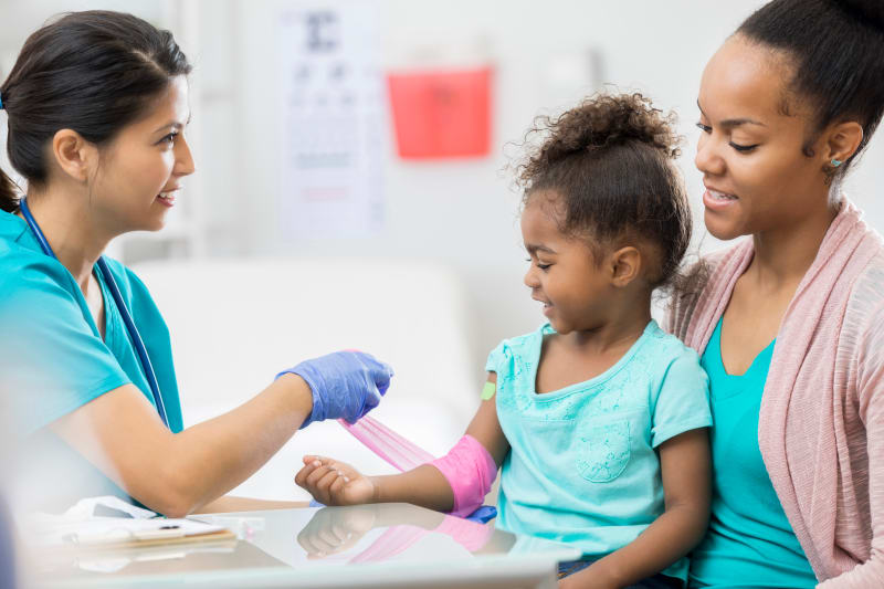 Mother holding Young Girl that is having blood drawn by Nurse.