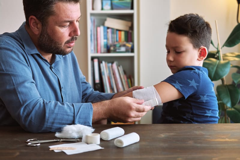 A father bandaging his son's wound.