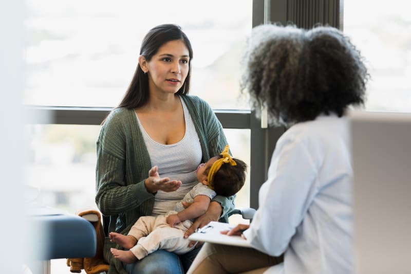 Mom holding Baby and talking to Doctor.