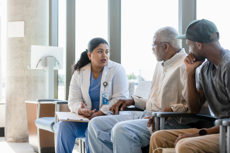Senior Man and Son listen to female Doctor.
