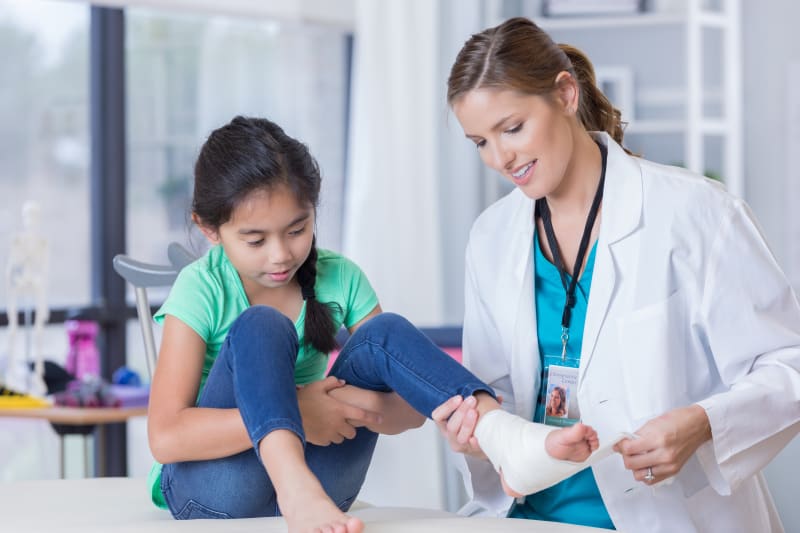 A child at a clinic getting her ankle injury wrapped by doctor. 