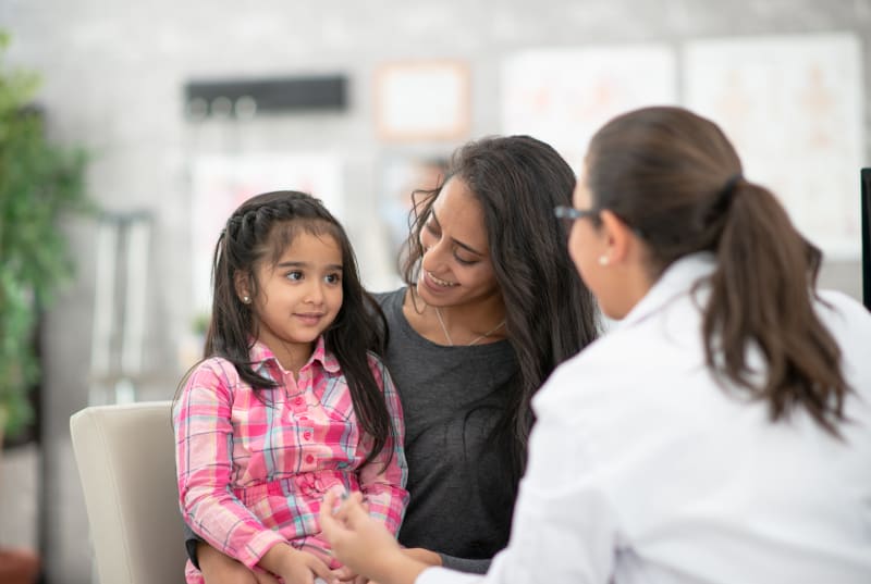 Young girl sitting on her mother's lap while doctor speaks to her.