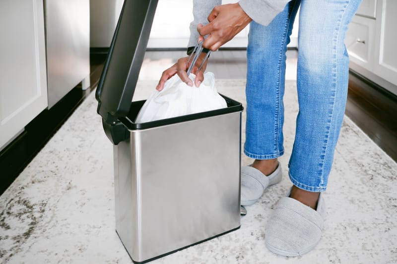 Woman cinching up white trash bag in kitchen garbage bin. 
