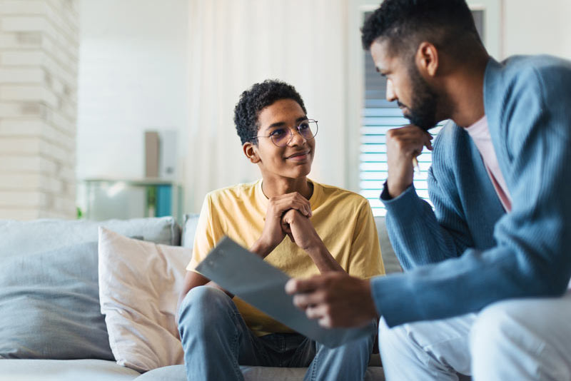 Teen boy talking with adult while relaxing on a couch.