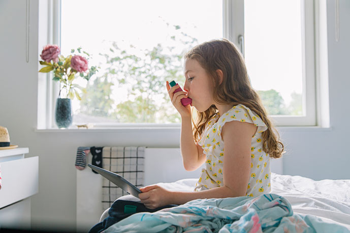 Young girl in exam room using an inhaler.