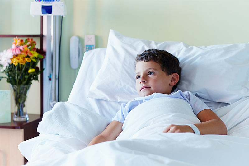 Thoughtful boy relaxing in bed at hospital ward.