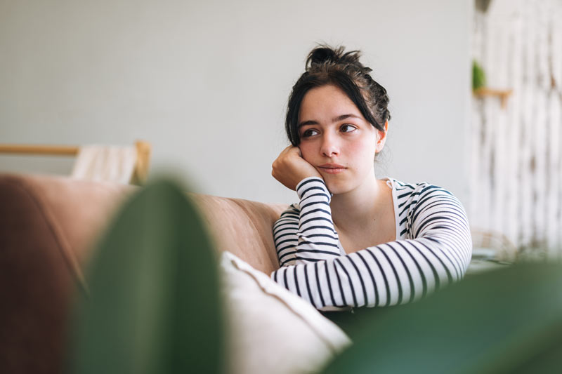 Uncomfortable teenage girl looking away and sitting in room at home.