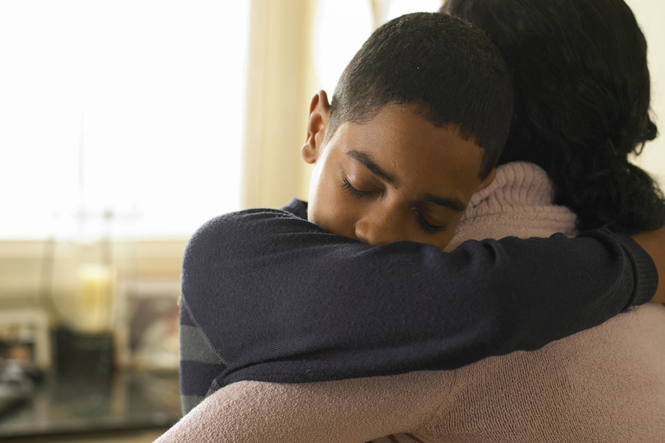 School age boy hugging his mother at home.