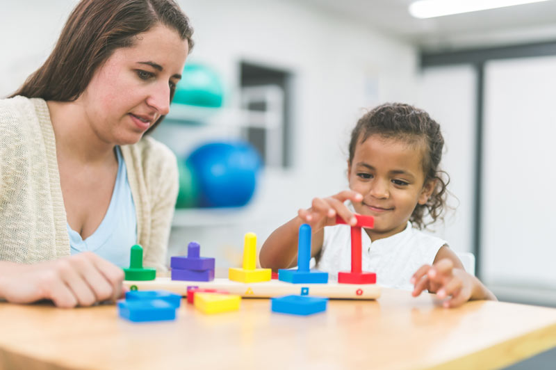 A female occupational therapist is doing rehabilitation with a child patient.